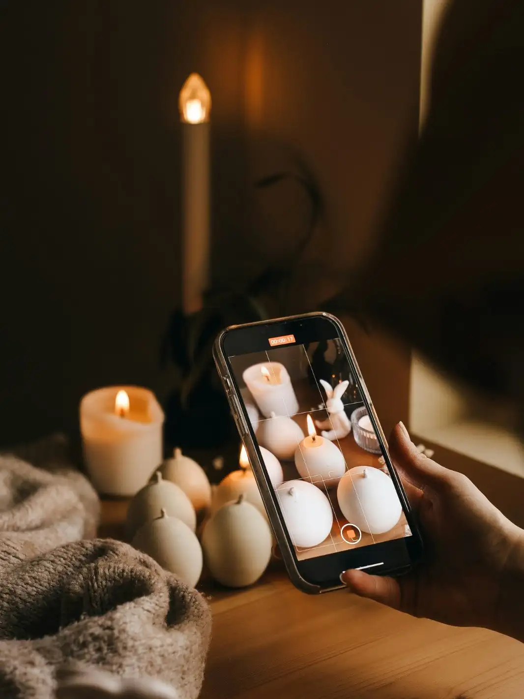 Mão filmando velas artesanais acesas com o celular, à luz de vela